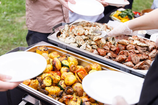 Food containers and stainless steel insulated containers with prepared meals for holiday buffets and event catering services. Hot baked potatoes, seasoned chicken, and meat