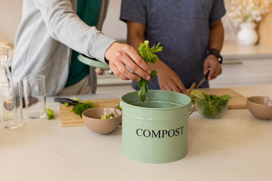 African American men dropping veg scraps at kitchen counter into green compost bin labeled COMPOST