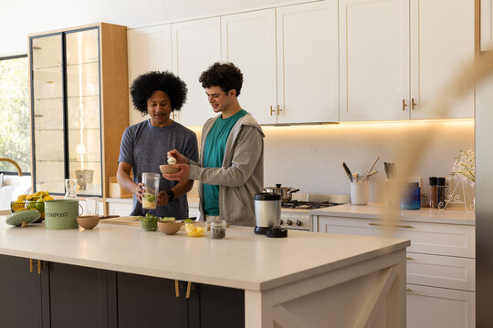 African American men steadying blender jar and adding ingredients at kitchen island with compost