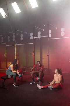 Diverse friends in workout clothes resting on rubber mat at gym with weight plates