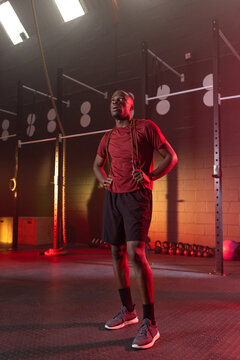 African man standing with jump rope draped on shoulders at CrossFit gym with kettlebells