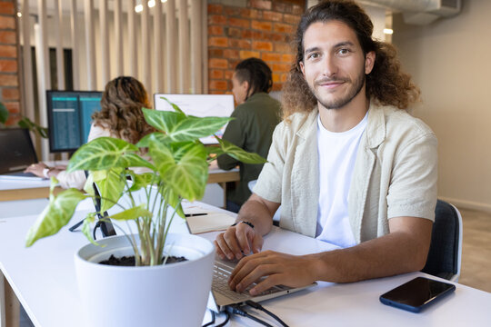 Diverse coworkers working at open-plan office around laptop, smartphone, potted plant, copy space