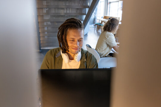 Male coworkers working in open office, one sitting at desk with monitor, white headset, green shirt