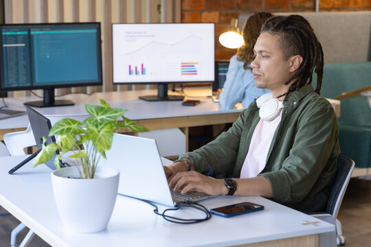 African American coworkers typing and analyzing code on laptop with monitors, smartphone, plant