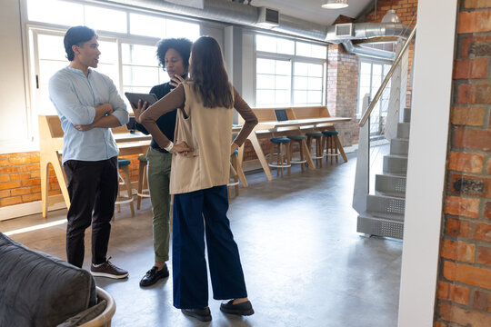 Diverse coworkers discussing tablet content near counter with laptops in modern office in workwear