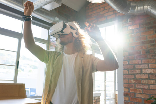 Adult male standing in loft workspace wearing white VR headset, reaching toward virtual interface