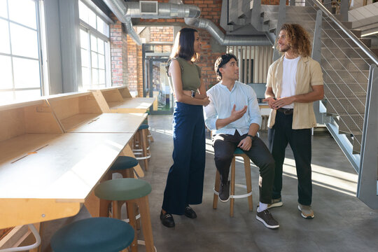 Diverse coworkers discussing ideas in loft with wooden workbench and big windows wearing casual