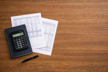 Obraz premium Top view of calculator, financial documents, notebook and pen on a wooden office desk with large copy space. Accounting, budgeting, tax calculation, financial planning and business paperwork concept.