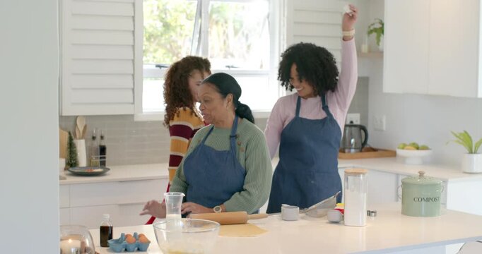African American female family preparing dough at kitchen island using rolling pin, dancing