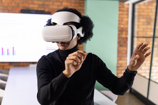 African American woman wearing white VR headset and black turtleneck gesturing at conference table