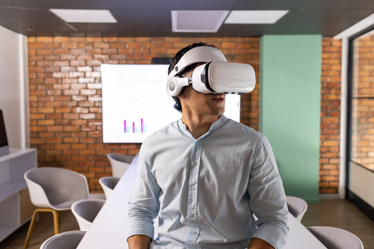 Asian man sitting at long white conference table wearing white VR headset light blue shirt