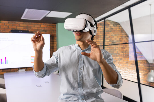 Asian man wearing VR headset, light blue shirt, interacting with virtual interface at meeting table