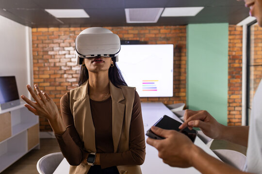 Diverse coworkers testing white VR headset in meeting room with wall screen and remote