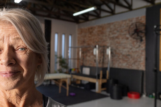 Senior female looking toward camera in Pilates studio, wearing light top, near reformer, copy space