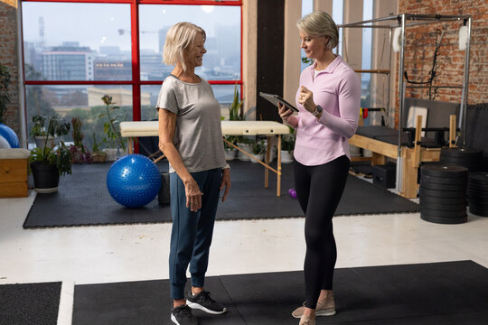 Senior woman and female trainer discussing exercises in pilates studio using tablet near blue ball