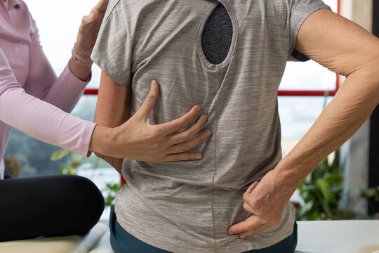 Senior woman and female therapist placing hands on gray cutout top getting back guidance at bench