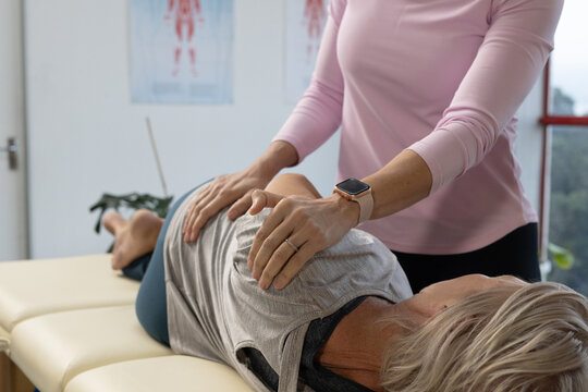 Female senior patient and female therapist doing therapy while lying on table by window smartwatch