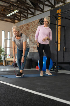 Female senior participant and coach stretching on blue mat in gym with red band in sportswear