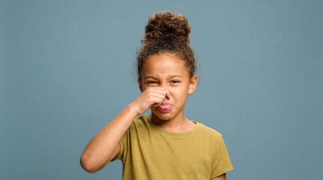 Young girl pinching nose and sticking out tongue with disgusted expression