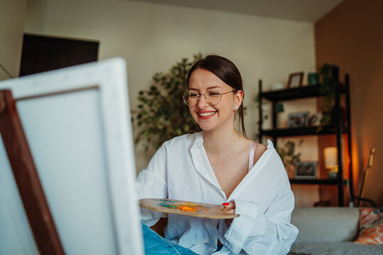 Young woman enjoying painting on easel at home studio