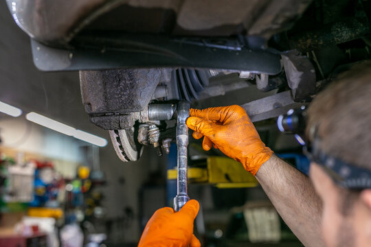 Mechanic using a ratchet spanner while working on the undercarriage of a vehicle, focusing on the front suspension and steering assembly during automotive repair and maintenance. The close-up workshop