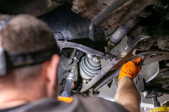 Mechanic using a ratchet spanner while working on the undercarriage of a vehicle, focusing on the front suspension and steering assembly during automotive repair and maintenance. The close-up workshop