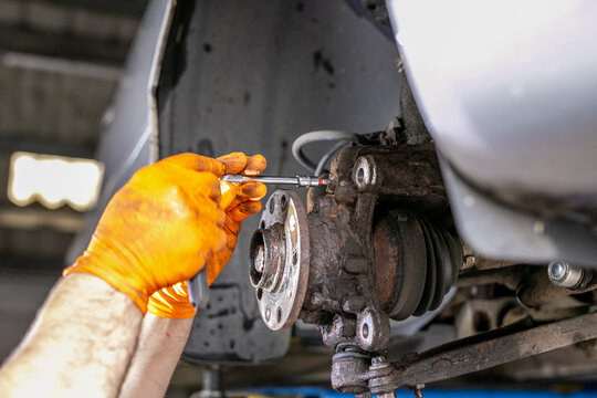 Close-up of a mechanic working on a vehicle&rsquo;s front suspension and steering knuckle assembly, separating or inspecting components around the lower ball joint area. The hands-on automotive repair scene