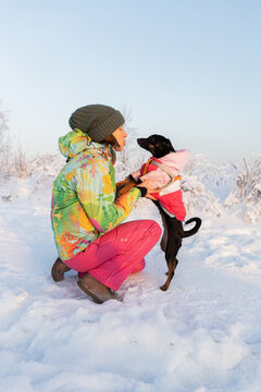 woman walking her small dog pauses to kiss her beloved pet. An active lifestyle. Enjoying quality time with the dog during a winter walk in a snow-covered park