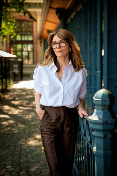 Elegant mature businesswoman in white blouse and brown pants standing between blue doors