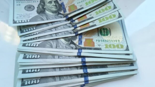A hand places a stack of $100 bills on a white table. Video footage about business and finance