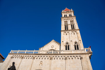 Obraz premium Tower of St. Lawrence Cathedral in Trogir, Croatia, featuring intricate stonework and a red-tiled roof against a clear blue sky