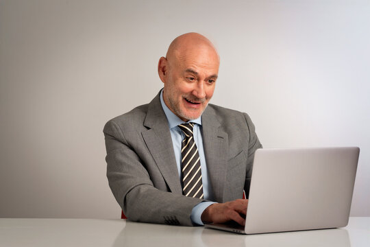 Confident senior man with laptop sitting against isolated background
