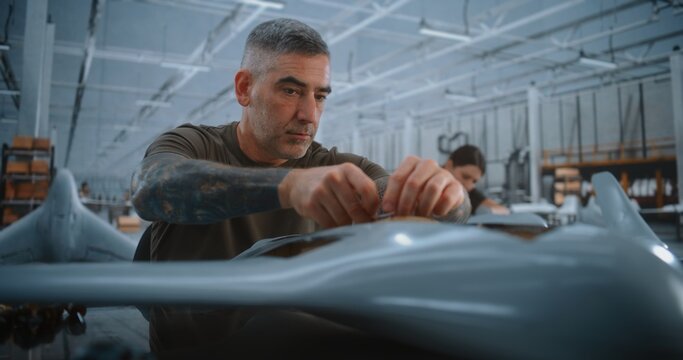 Experienced Male Technician Carefully Routes Electrical Wiring Through Fuselage of Fixed Wing UAV During Detailed Assembly in Large Modern Aerospace Manufacturing Facility. Wiring Installation.