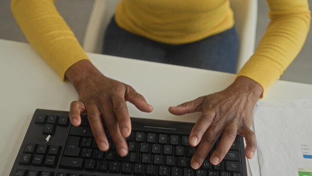 Woman rubbing wrist and grasping hands over a keyboard at a desk inside a building while pausing from typing; discomfort relief.