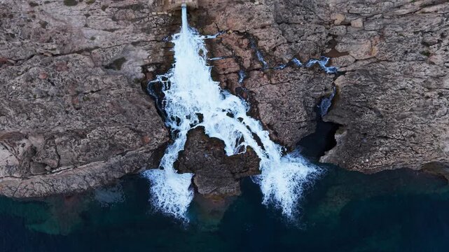 Industrial wastewater cascades from a reverse osmosis desalination plant outlet down rugged limestone cliffs into the sea, captured by drone above Ghar Lapsi, Malta.