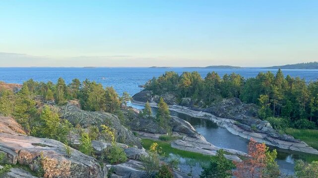 Stunning view from the highest point of the Ladoga skerries on Honkasalo island in the summer windy day, showcasing a rocky coastline with vibrant green trees and tranquil blue waters. Karelia, Russia