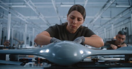 Young Female Worker Assembling Drone Components at Industrial Workbench, Representing Advanced...