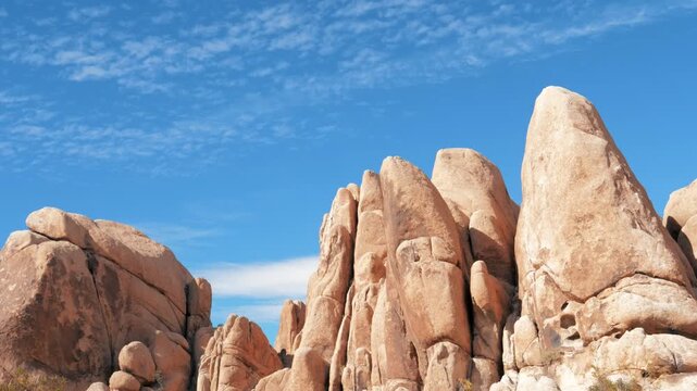 High granite rock formations typical of joshua tree national park with wispy white clouds moving quickly across brilliant blue sky, highlighting rugged desert landscape of california. Timelapse video