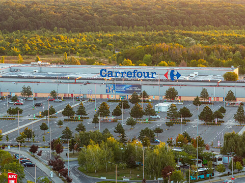 Bucharest, Romania Elevated morning view of Carrefour hypermarket Baneasa with vast parking lot bathed in warm golden sunrise light and lush trees.
