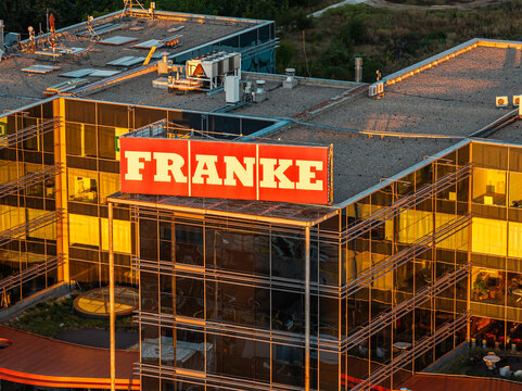 Bucharest, Romania Franke commercial logo on the modern glass facade of a corporate office building bathed in warm morning sunrise light.