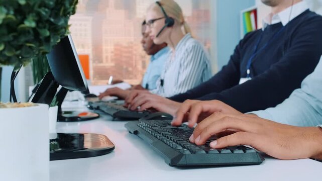 Three employees working at computers in a modern corporate office. One woman wearing headset is on a call while others type on keyboards at their desks.