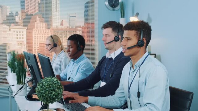 A diverse group of call center agents wearing headsets and professional attire working together at their desks in a modern corporate office environment.
