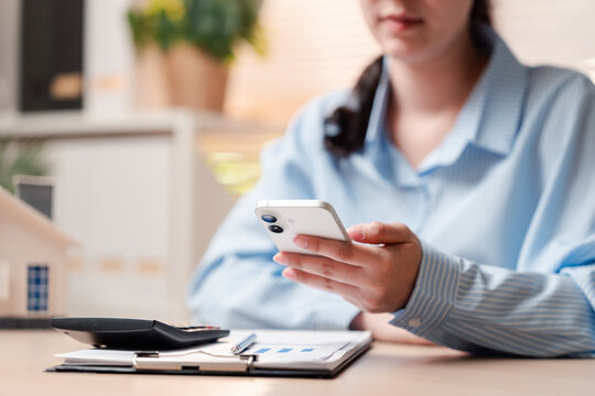 Real estate property investment mortgage loan and finance. Woman hands holding smartphone with calculator and house model on desk.