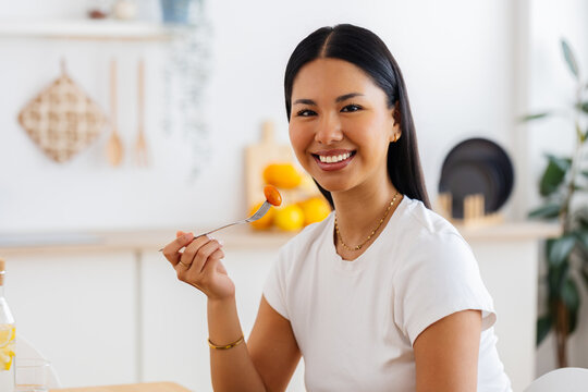 Portrait of young millennial Latin American woman eating fresh salad in the kitchen at home. Healthy lifestyle concept
