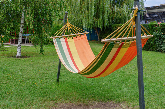 A colorful striped hammock hangs on metal poles in a green backyard garden.