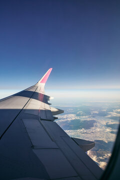 Airplane Wing Flying Above Clouds and Mountains Against Blue Sky