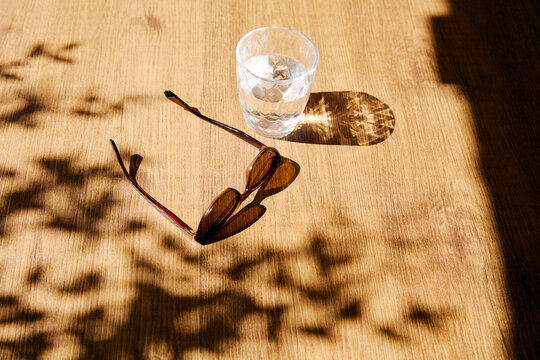 Sunglasses and a Glass of Water on Wooden Table in Sunlight