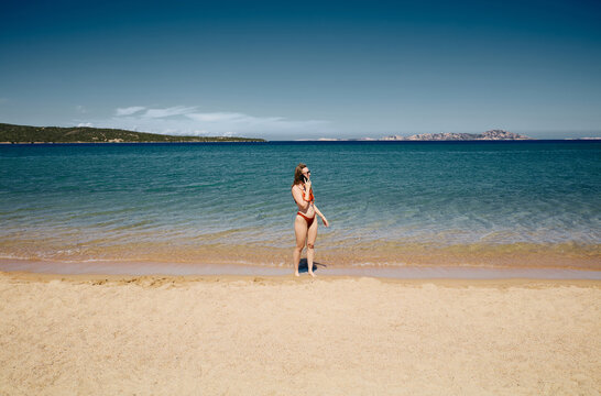 Woman in Bikini Talking on Smartphone on a Sunny Beach by the Sea