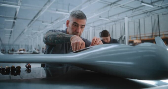 Experienced Male Technician Installs Internal Hardware and Routes Connections Through Unmanned Aircraft Body While Working on Large Modern Aerospace Production Line. Concept of Production Environment.
