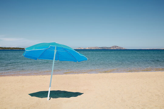 Blue parasol on empty sandy beach against sea and clear sky